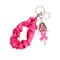 Hot pink satin scrunchie wristlet keychain looped open, with silver-tone key ring, swivel lobster clasp and enamel brown-haired woman charm wrapped in a pink ribbon