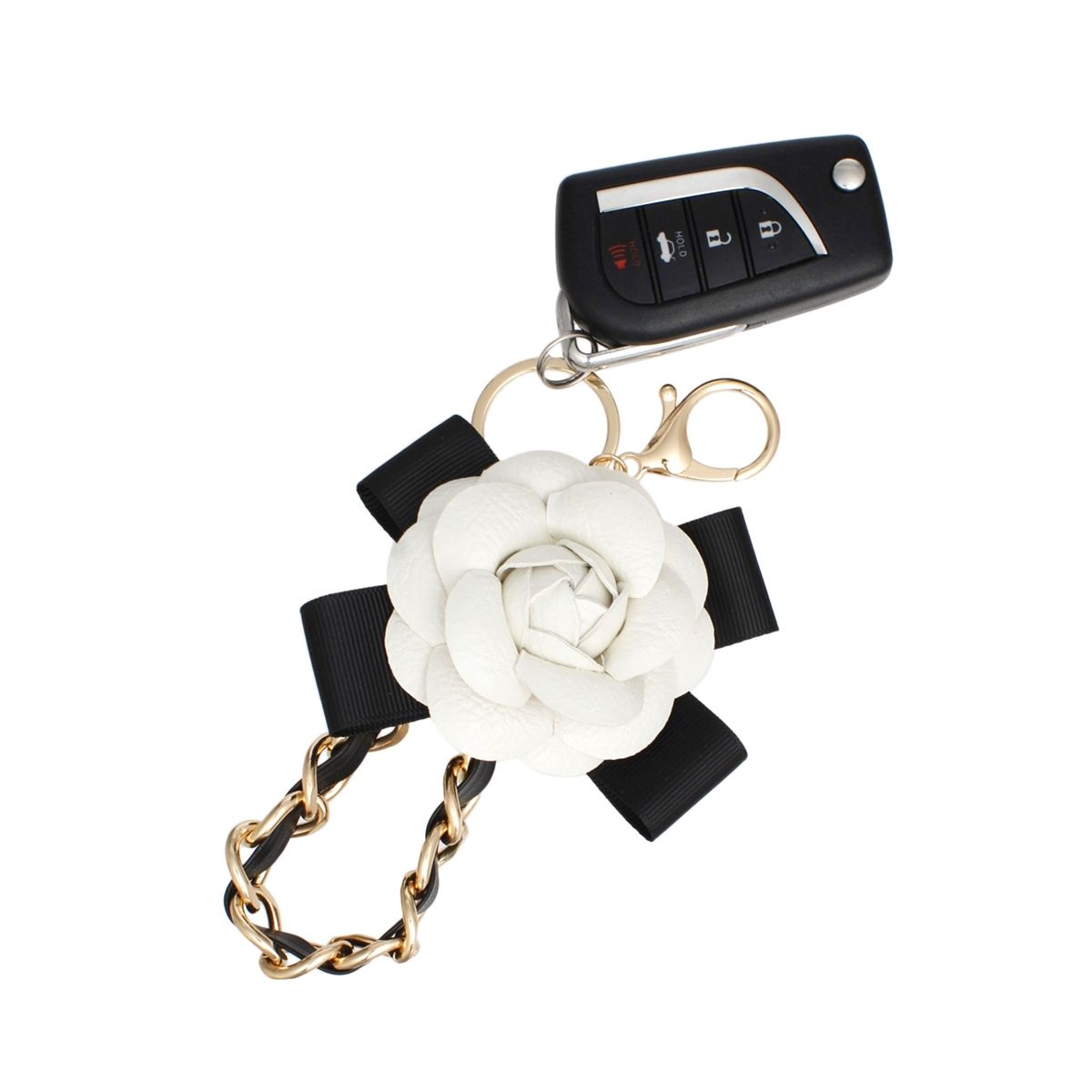 White 3D vegan leather camellia flower bag charm with black grosgrain ribbon bow and chunky gold chain woven with black faux leather, displayed on white hexagon stand with pink background