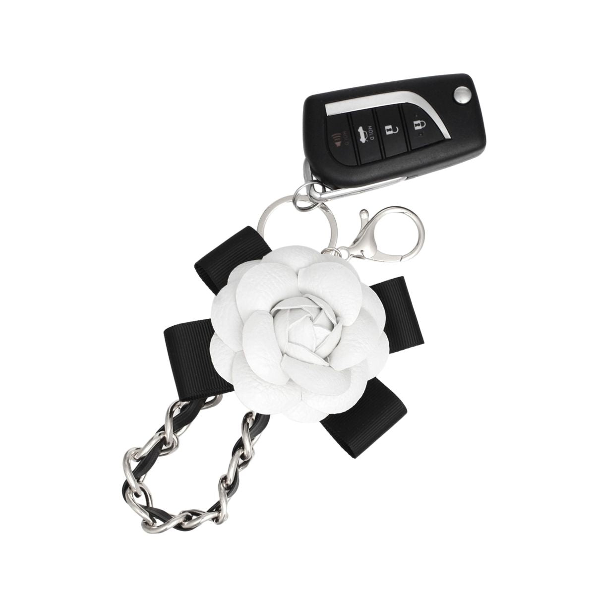 White 3D vegan leather camellia flower bag charm with black grosgrain ribbon bow and silver chain, shown attached to a car key fob with rhodium lobster clasp and split keyring on white background