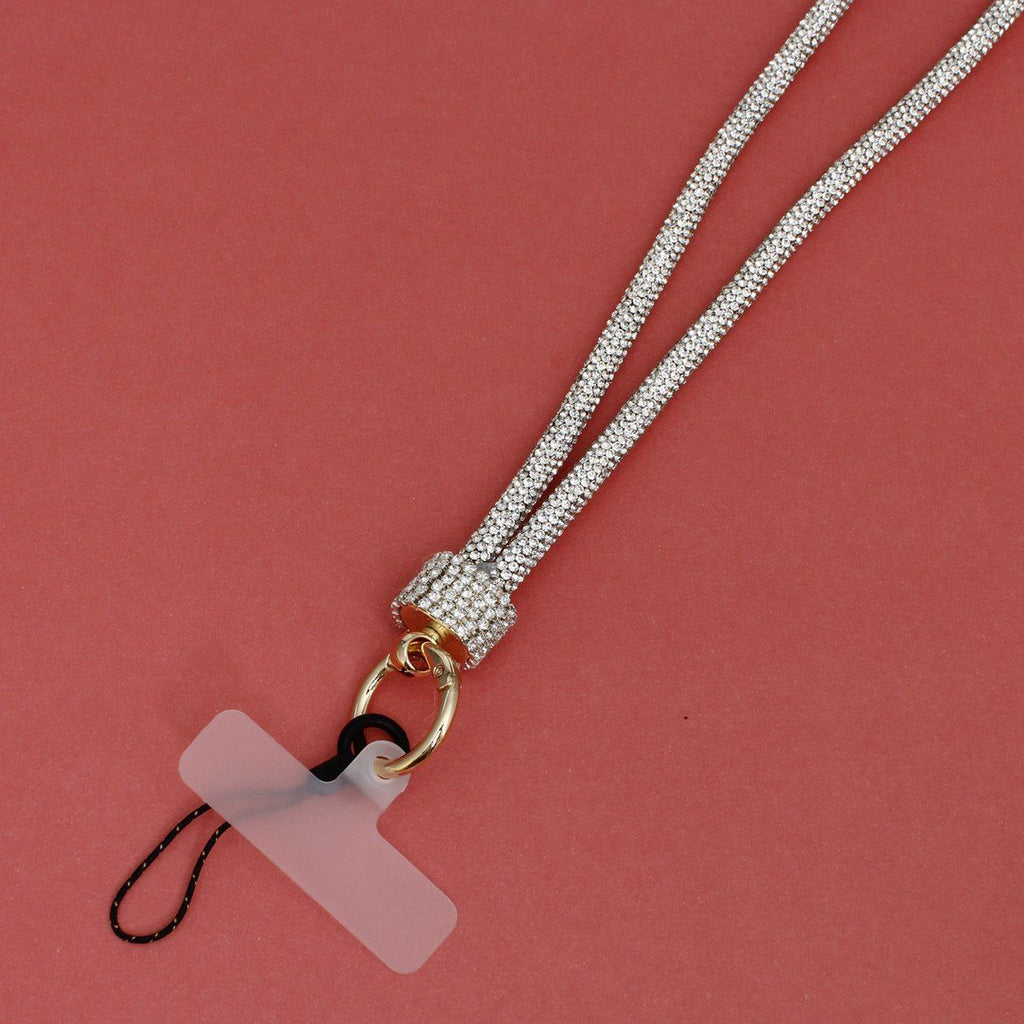 Close-up detail of clear rhinestone-encrusted tube phone lanyard on red background, showing clear rhinestone barrel slide, round gold push clasp with black cord loop, and clear plastic card insert