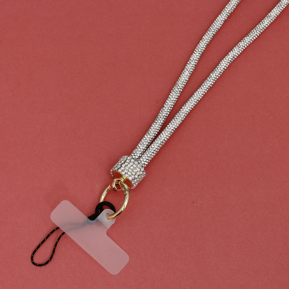 Close-up detail of clear rhinestone-encrusted tube phone lanyard on red background, showing clear rhinestone barrel slide, round gold push clasp with black cord loop, and clear plastic card insert