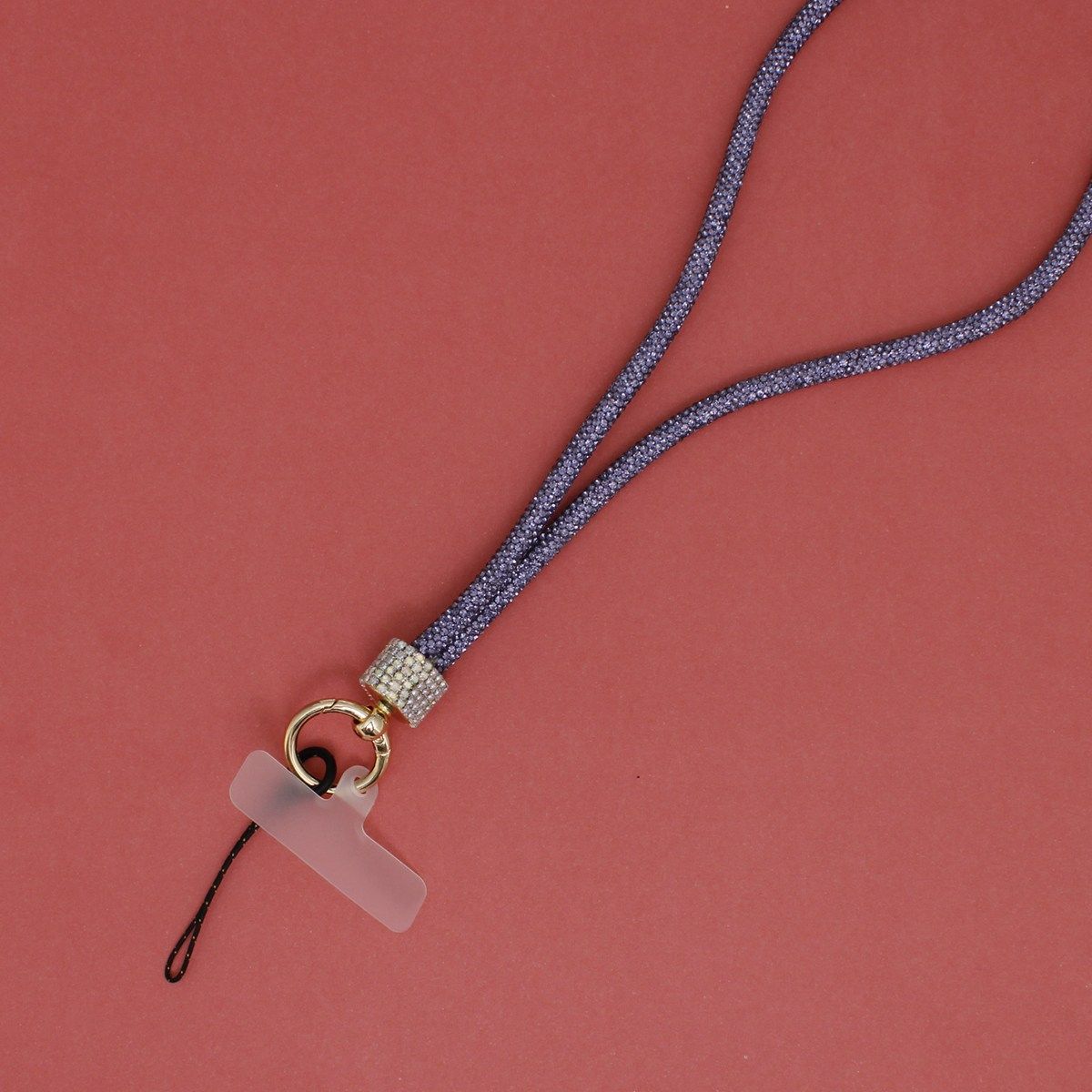 Close-up detail of purple rhinestone-encrusted rope phone lanyard on red background, showing double-strand purple rhinestone rope, clear rhinestone barrel wrap, round gold carabiner clasp, clear plastic card insert, and black cord loop