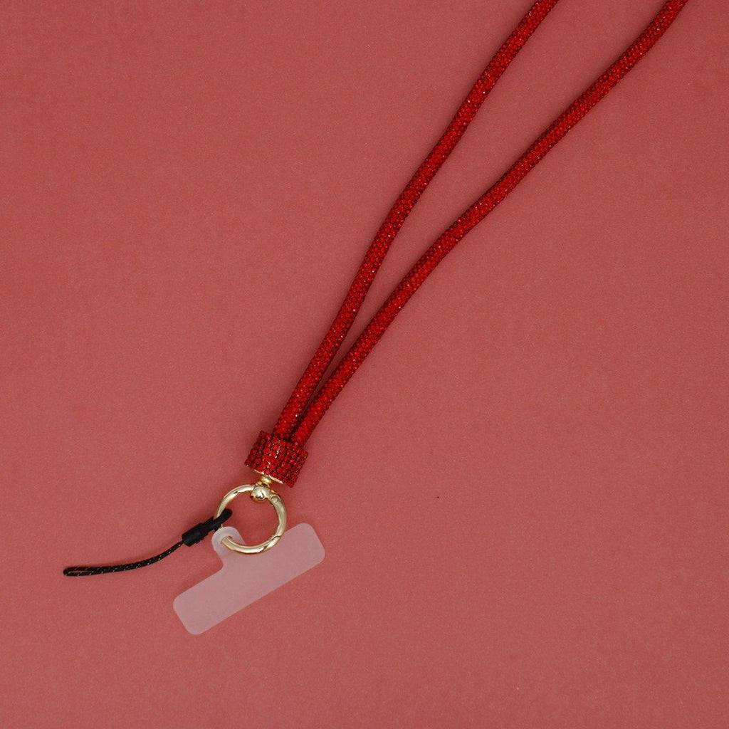 Close-up detail of red rhinestone-encrusted tube phone lanyard on pink background, showing red rhinestone barrel slide, round gold push clasp with black cord loop, and clear plastic card insert