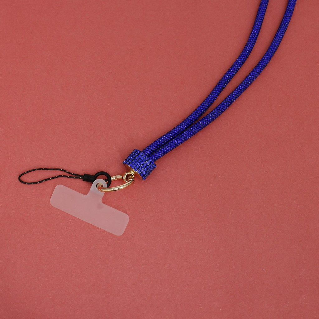 Close-up detail of royal blue rhinestone-encrusted rope phone lanyard on pink background, showing blue rhinestone barrel wrap, round gold lobster clasp, black cord loop, and clear plastic card insert