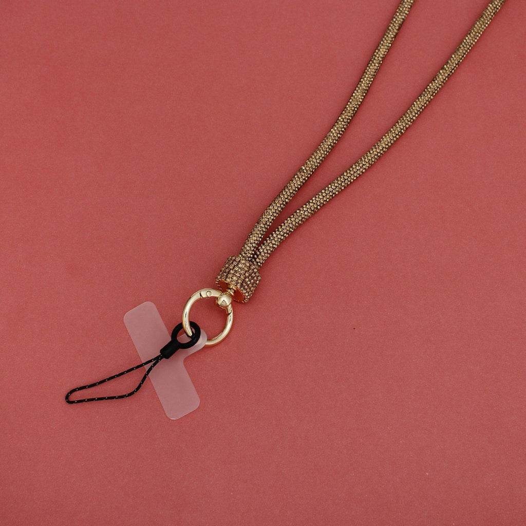 Close-up detail of topaz gold rhinestone-encrusted tube phone lanyard on pink background, showing gold rhinestone barrel slide, round gold push clasp with black cord loop, and clear plastic card insert