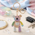 Multicolor rhinestone articulated teddy bear keychain with heart chest detail and gold lobster clasp on pastel surface