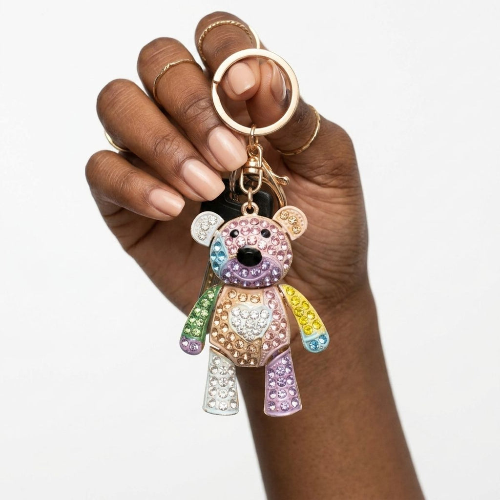 Hand holding multicolor rhinestone teddy bear bag charm keychain with heart detail and gold hardware