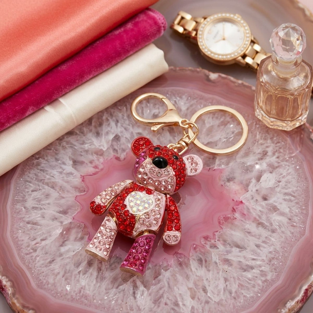 Red and pink rhinestone articulated teddy bear keychain with heart chest detail and gold lobster clasp on pink agate tray