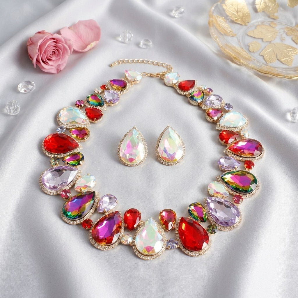 Light multicolor crystal collar necklace and matching teardrop stud earrings in gold-tone setting, displayed on white satin with pink rose and scattered crystals