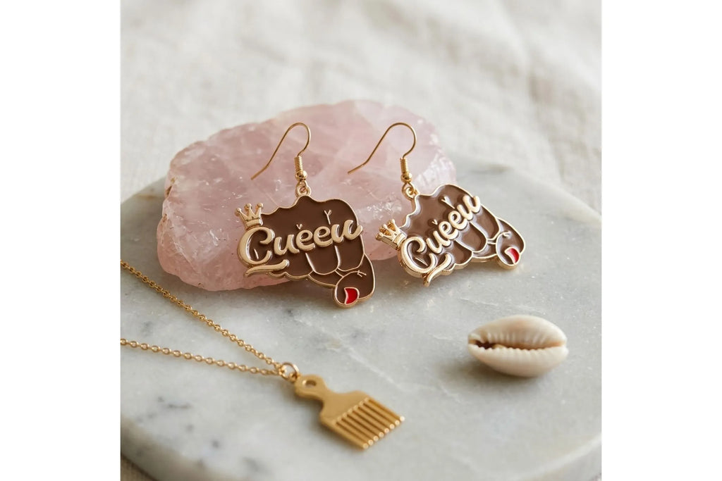 Pair of brown epoxy raised fist "Queen" crown gold fish hook earrings displayed on pink rose quartz crystal on white marble surface, alongside gold afro pick pendant necklace and cowrie shell