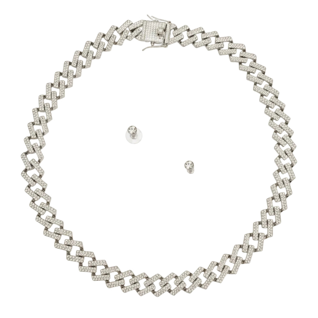 Overhead flat lay of a wide silver tone fully pave clear rhinestone square Cuban chain link necklace arranged in a circle on a white background. A square push-lock box clasp covered in clear rhinestones with a safety latch is visible at the top. Two small clear rhinestone round stud earrings with clear rubber butterfly post backings are displayed inside the necklace loop.
