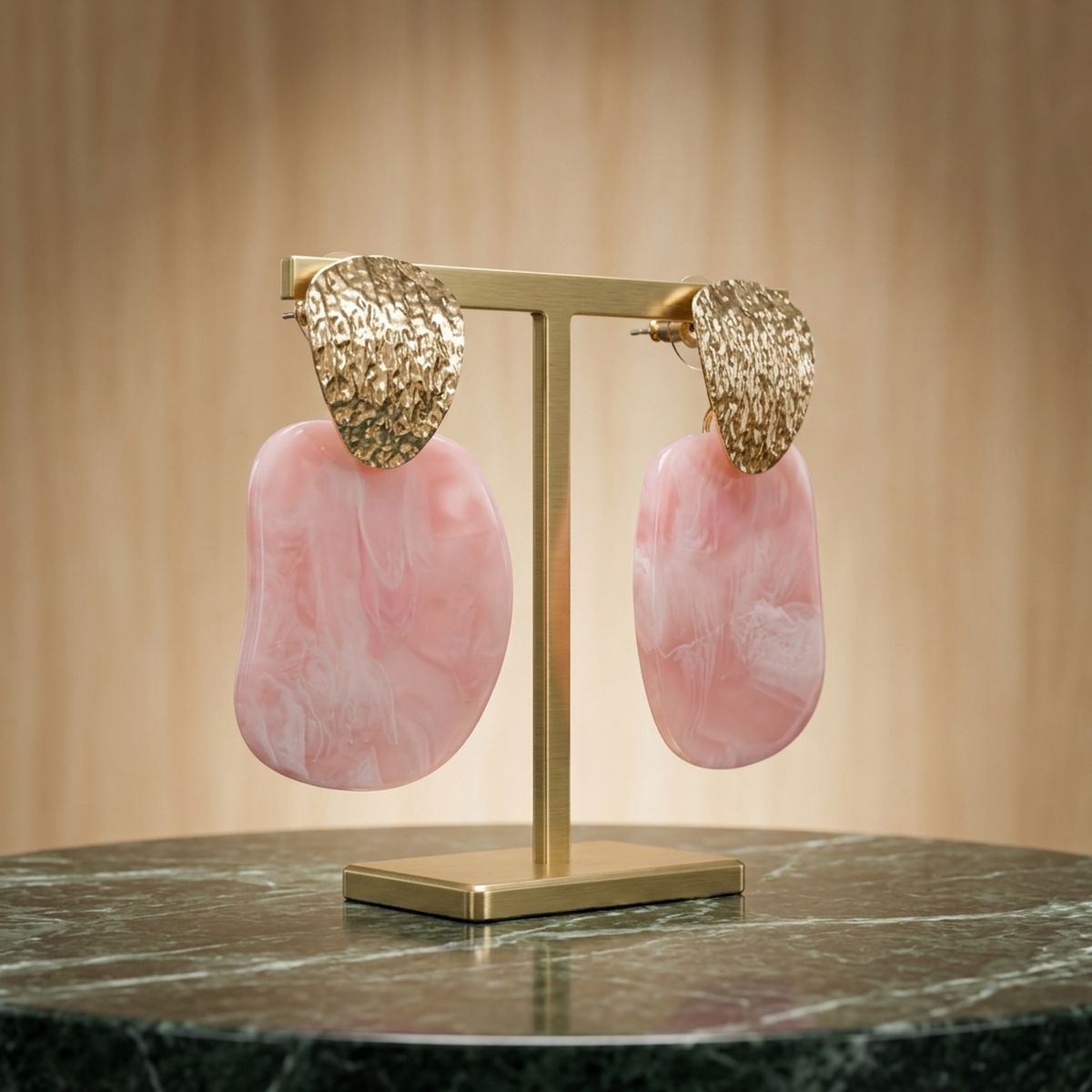 Light pink marbled resin drop earrings with hammered gold-tone tops displayed on a gold jewelry stand