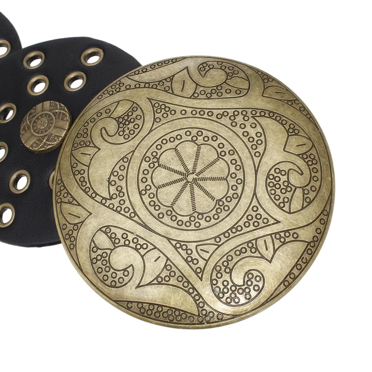 Closeup of large engraved distressed gold round concho buckle with intricate floral and paisley etched pattern, black vegan faux leather disc panel with gold grommet punch-out details visible in background, white background