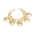 Overhead flat lay of a chunky gold tone double oval link chain charm bracelet on a white background. Five oversized puffy hollow polished gold heart charms dangle from the interlocking double oval links. A round ring and toggle bar closure is visible at the top right of the bracelet.