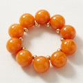 Orange swirled bubble bead bracelet with small gold-tone spacers arranged in a circle on cream textured fabric