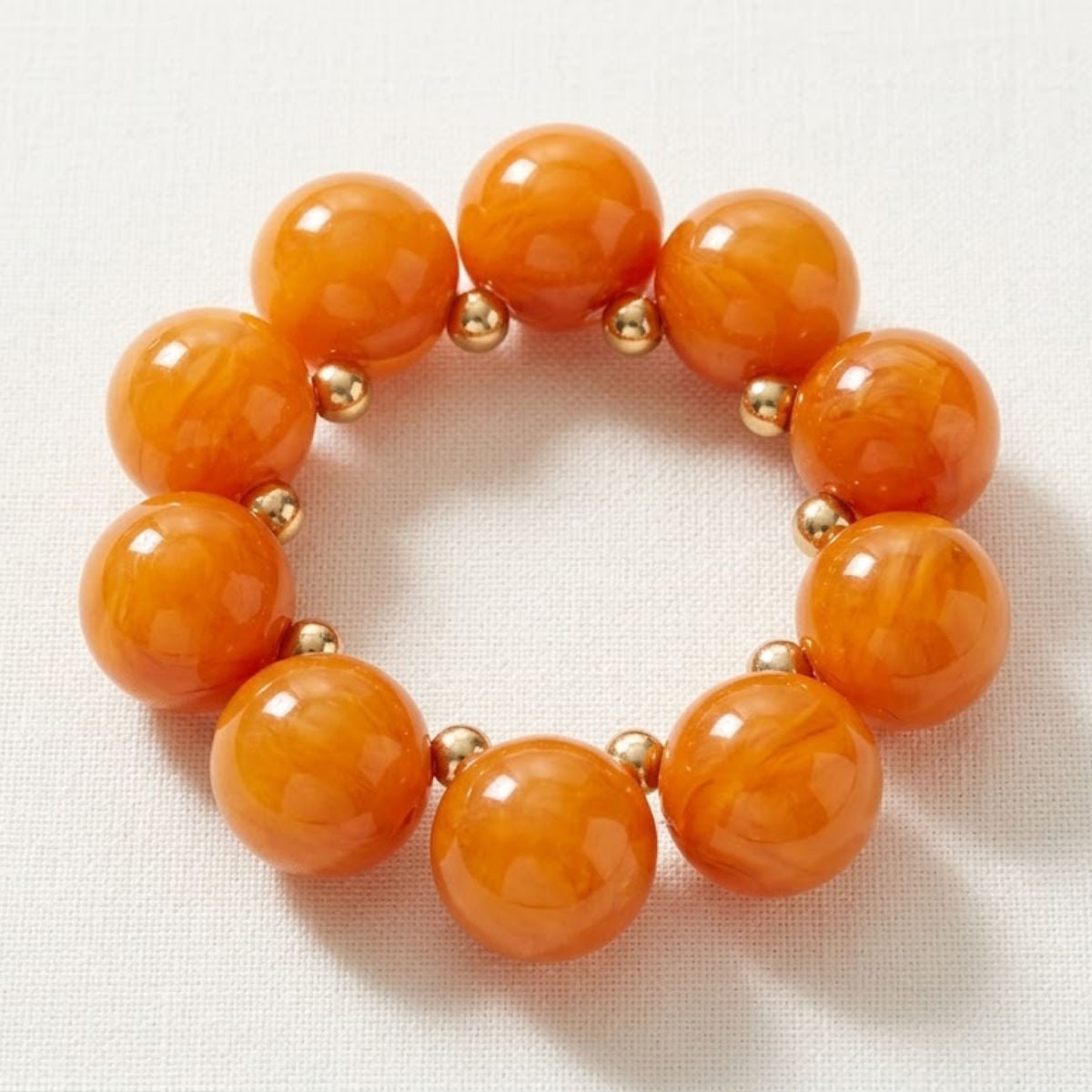 Orange swirled bubble bead bracelet with small gold-tone spacers arranged in a circle on cream textured fabric