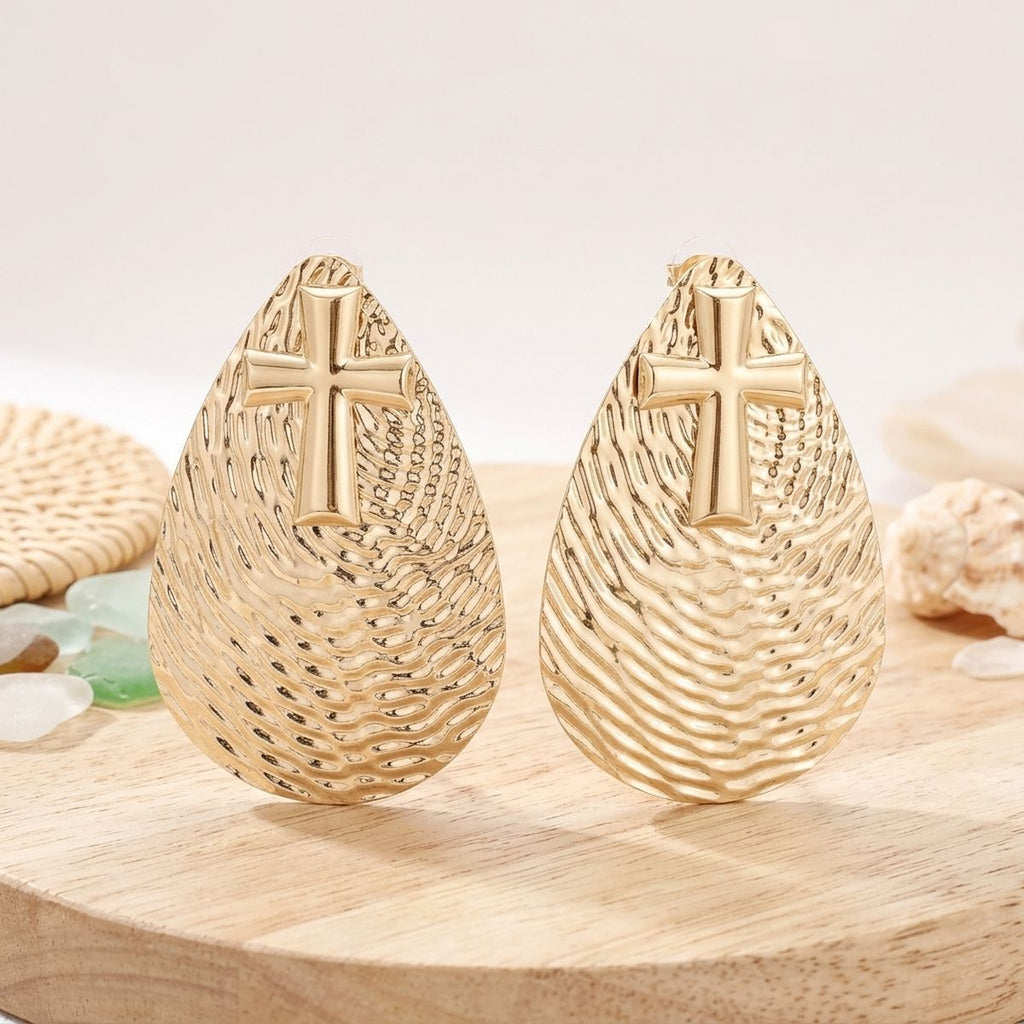 Pair of oversized gold-tone ripple-textured teardrop earrings with raised cross emblems