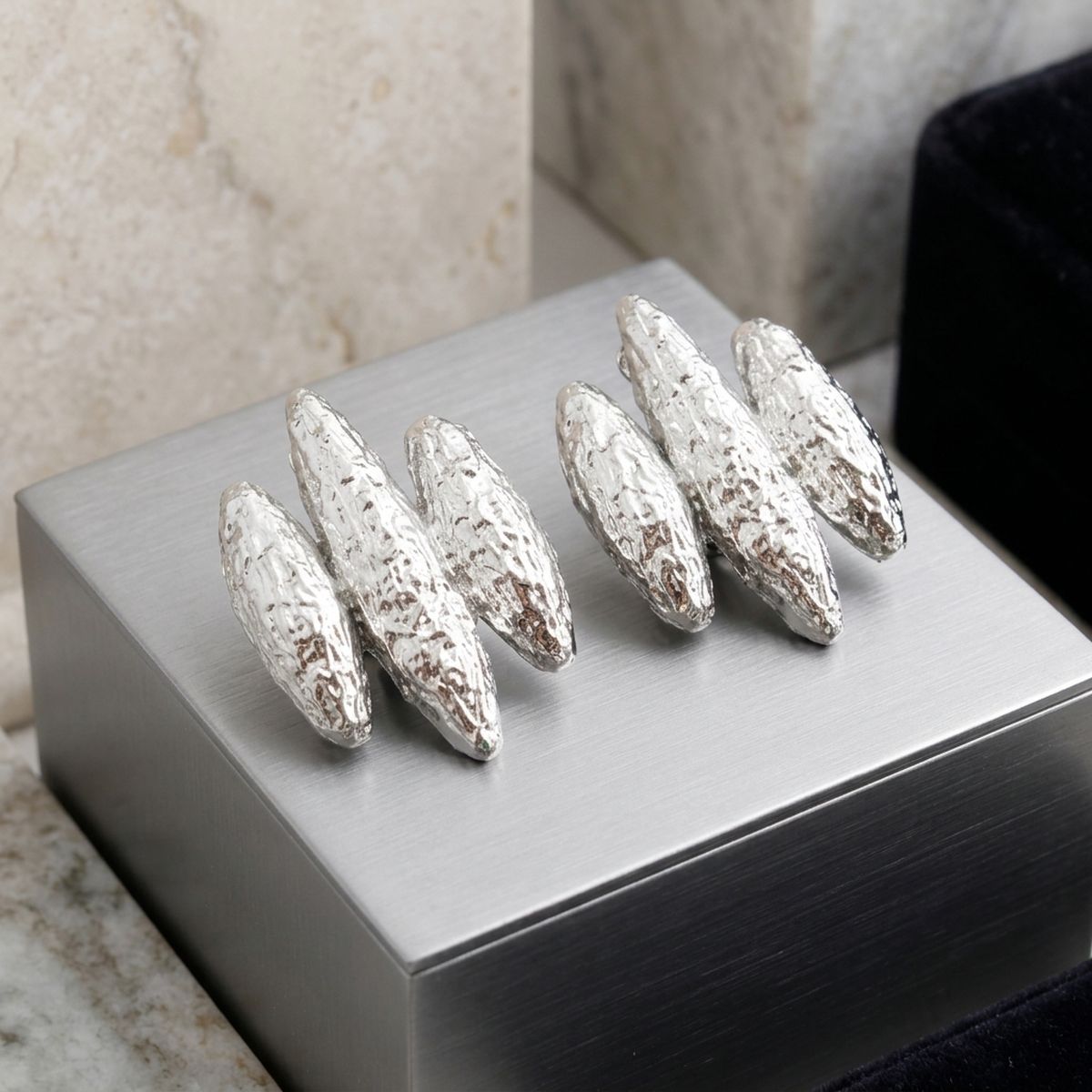 Silver textured triple-rib clip-on earrings displayed as a pair on a white jewelry box.