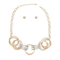 Overhead flat lay of a mixed metal multi-wire open ring collar necklace on a white background. The collar section features five linked oversized multi-wire open rings in gold, rose gold, and silver tone. A gold tone oval link chain with lobster clasp and 3-inch extender is visible at the top. Two small gold tone ball stud earrings with butterfly post backings are displayed above the necklace.