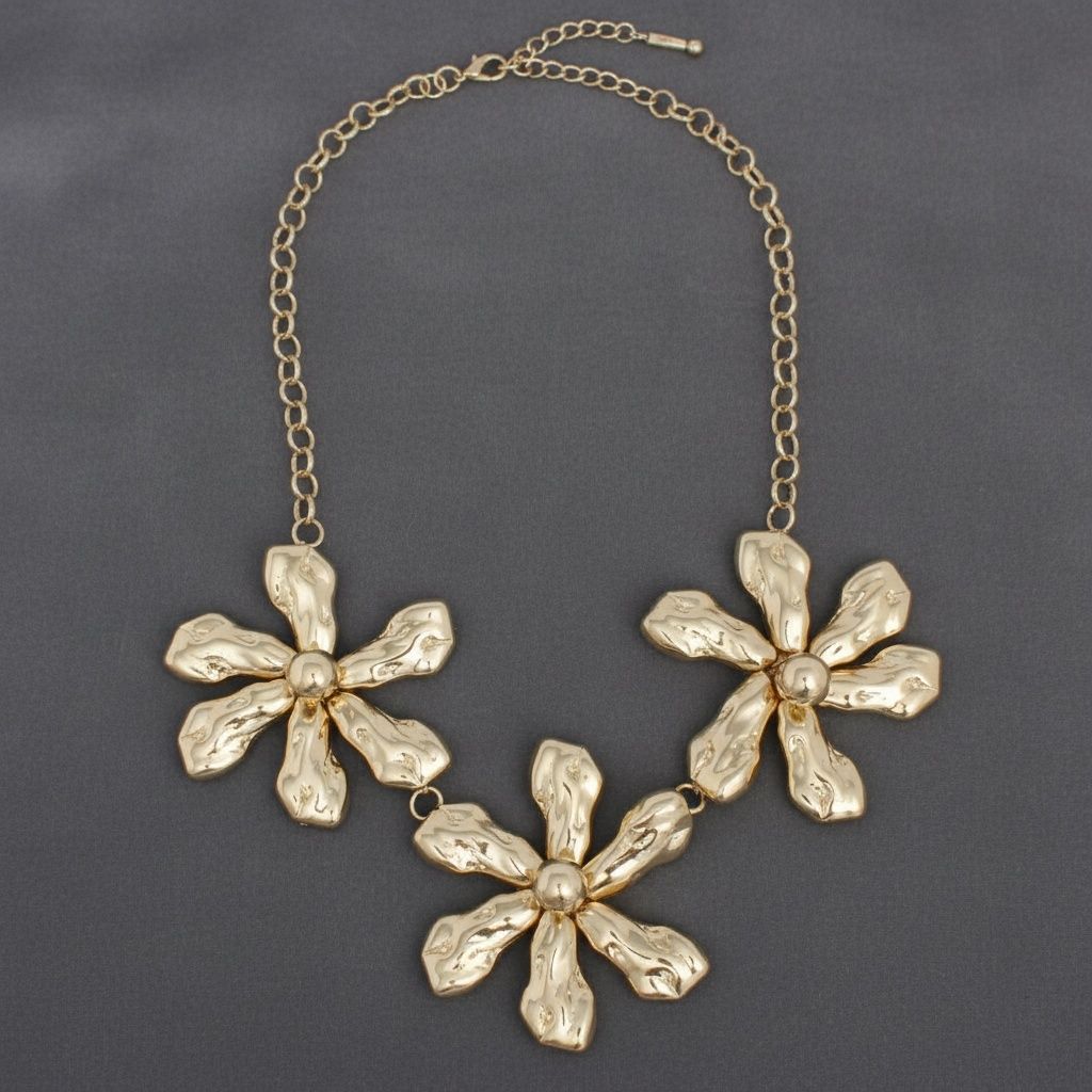 Gold-tone chunky triple floral bib necklace with hammered organic petal texture, raised dome centers, and gold oval link chain with lobster clasp extension, displayed on grey background