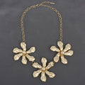 Gold-tone chunky triple floral bib necklace with hammered organic petal texture, raised dome centers, and gold oval link chain with lobster clasp extension, displayed on grey background
