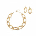 Overhead flat lay of an oversized diamond cut geometric open link chain necklace in matte gold tone arranged in a circle on a white background, with a lobster clasp and 2-inch extender chain visible at the top. Two matching double open geometric diamond-shaped drop earrings with fish hook backs are displayed to the upper right.