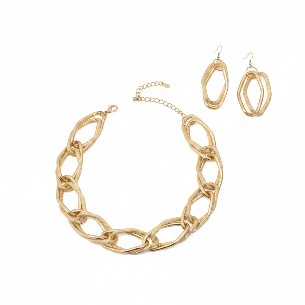Overhead flat lay of an oversized diamond cut geometric open link chain necklace in matte gold tone arranged in a circle on a white background, with a lobster clasp and 2-inch extender chain visible at the top. Two matching double open geometric diamond-shaped drop earrings with fish hook backs are displayed to the upper right.