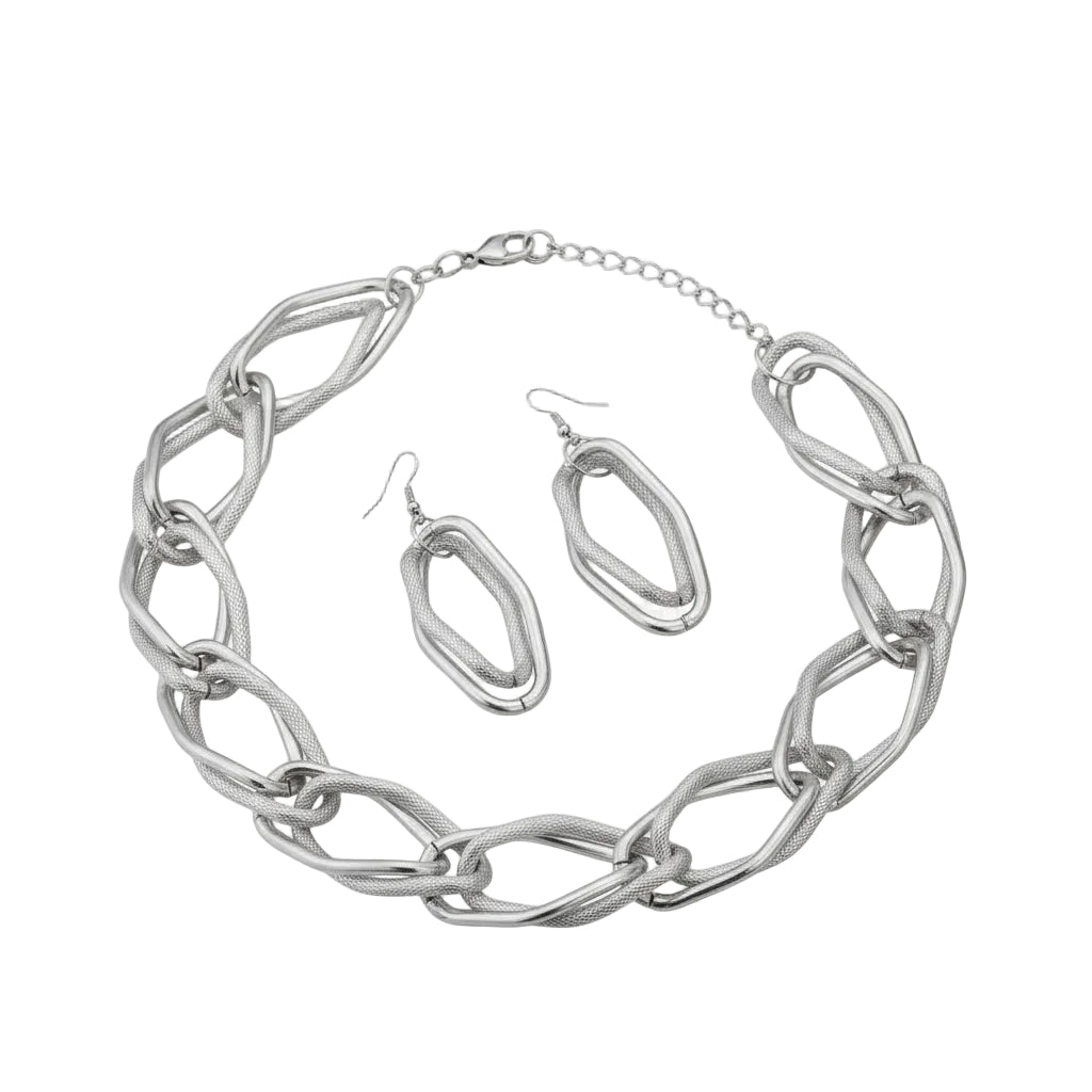 Overhead flat lay of an oversized diamond cut geometric open link chain necklace in rhodium silver tone arranged in a circle on a white background, with a lobster clasp and 2-inch extender chain visible at the top right. Two matching open oval drop earrings with fish hook backs featuring alternating smooth polished and textured diamond cut finishes are displayed in the center of the necklace loop.
