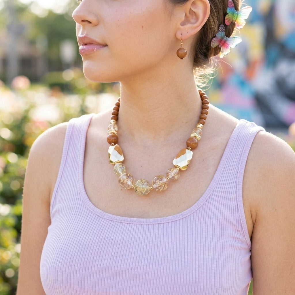 Model wearing a brown beaded necklace with clear gold-flake resin beads, gold-tone accents, and matching drop earrings
