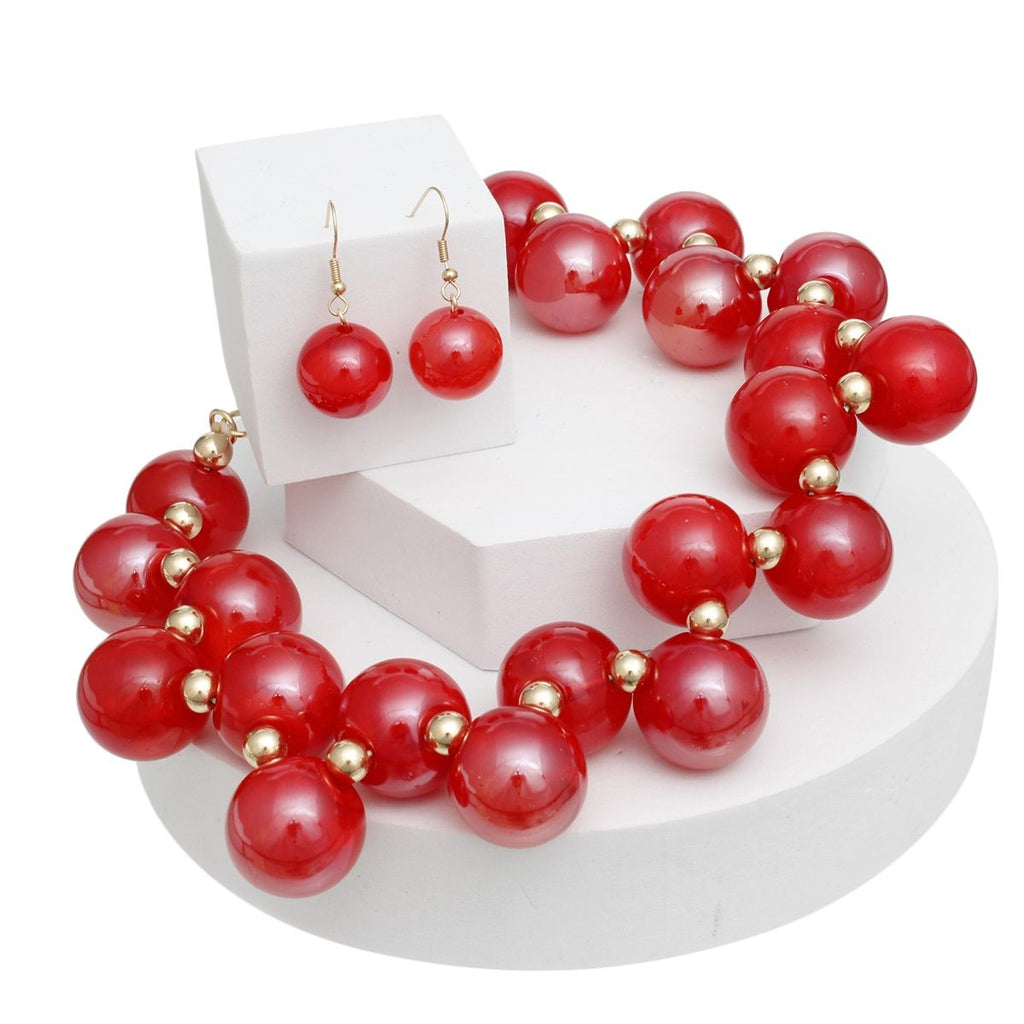 Red swirled bubble bead necklace with gold-tone spacers draped around white display blocks, with matching red bead fishhook earrings on an upright block.