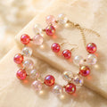 Red and pink iridescent bubble-bead necklace with gold spacers and matching drop earrings arranged on cream fabric