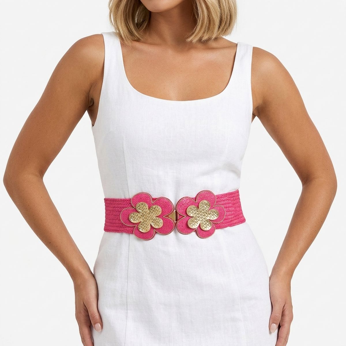 Fuchsia wide woven raffia stretch belt worn on woman's waist over white sleeveless scoop neck linen dress, double gold basket-weave flower hook closure at center with fuchsia raffia petals and gold trim edging, white background