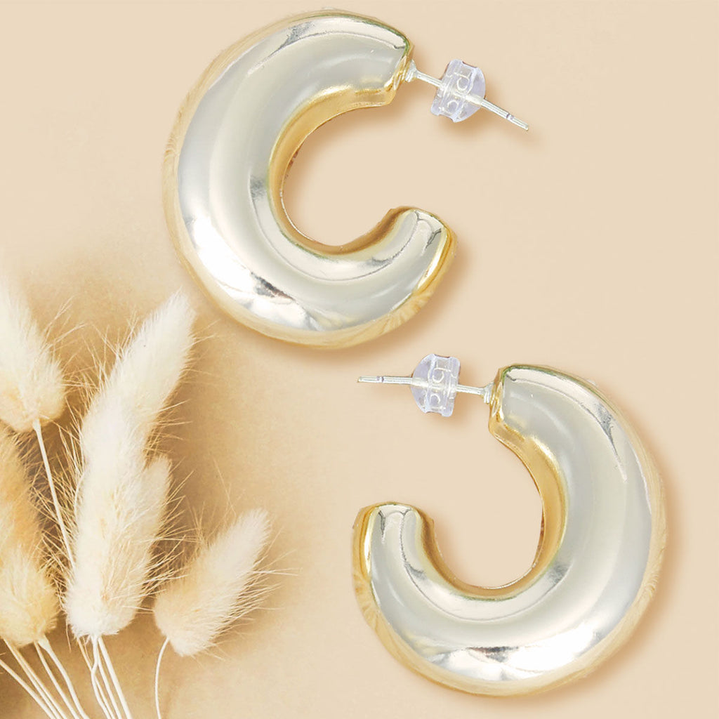 Two 14K gold plated chunky puffy hoop earrings with clear push back closures displayed on beige background with dried pampas grass, showing high-polish gold tube hoop body and post detail