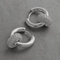 Two 14K white gold plated CZ pavé ring huggie hoop earrings displayed on gray textured surface, close-up showing polished silver hoop body and fully pavé-set cubic zirconia ring charm detail