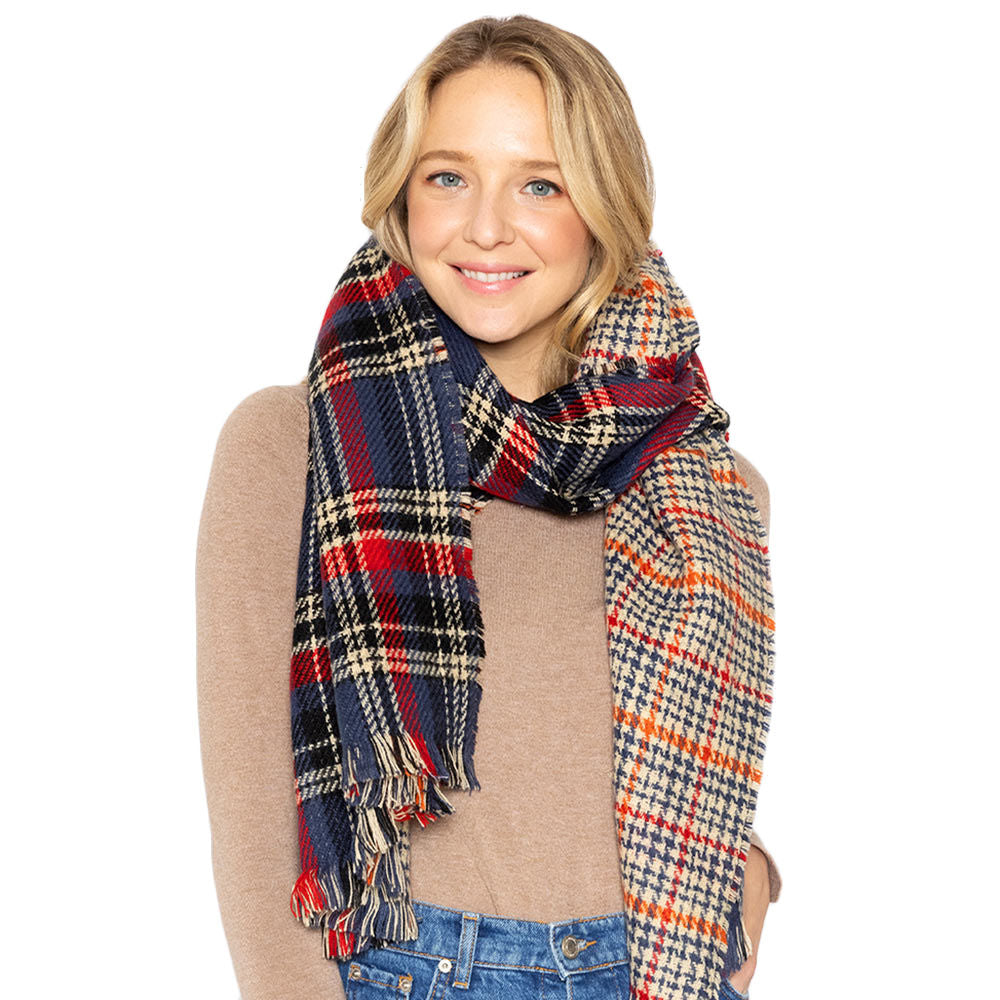 Model wearing a reversible navy, red, and cream plaid scarf over a beige sweater and blue jeans, with the cream-and-navy houndstooth reverse and fringed ends visible