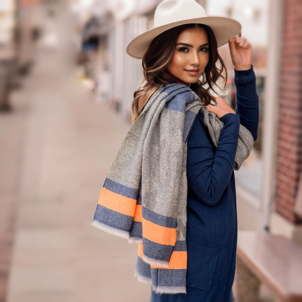 Model in a navy outfit and cream wide-brim hat carrying a gray camouflage scarf over her shoulder, with blue and orange stripes visible against a blurred city background