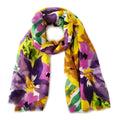 Purple, pink, and yellow watercolor floral scarf loosely looped against a white background, showing green leaves and fine frayed ends
