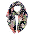 Black tropical floral scarf loosely looped against a white background, showing green leaves, pale fronds, and pink and coral flowers