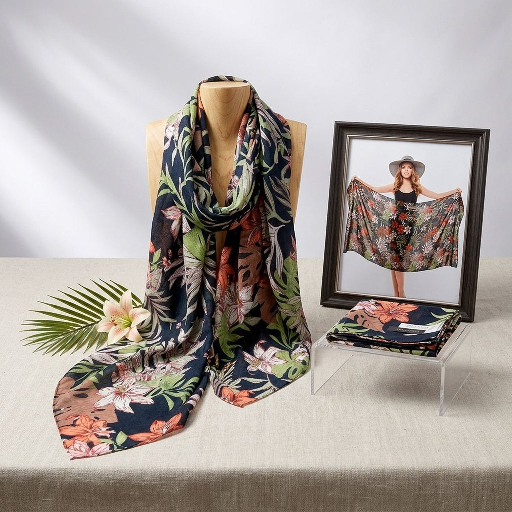 Tropical floral scarf draped around a wooden display bust beside a flower, palm frond, folded scarf, and framed photo of a model holding the wrap open