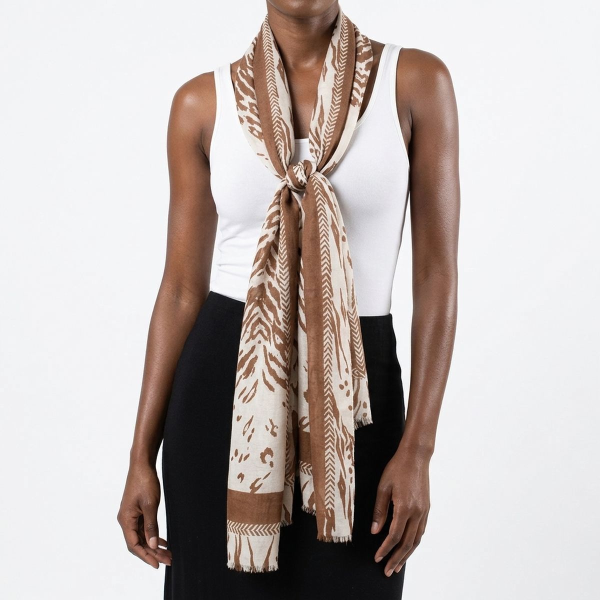 Model wearing a brown-and-beige animal print scarf tied loosely over a white sleeveless top and black trousers against a pale background