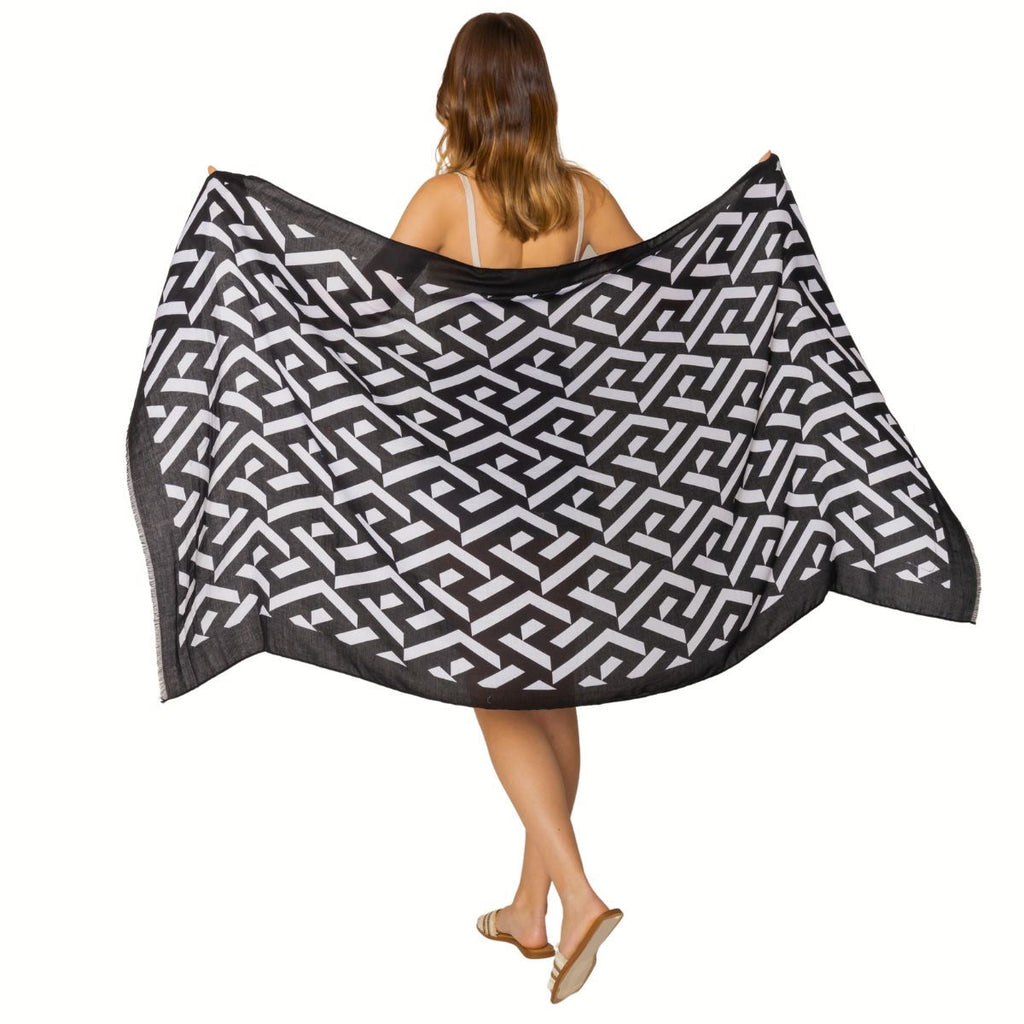 Rear view of a model holding a black-and-white geometric wrap spread wide behind her against a white background