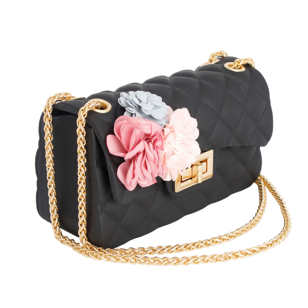 Angled view of black quilted jelly crossbody bag showing its side depth, pastel flower appliqués, gold-tone twist lock, and chain strap draped across a white background