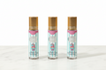 Three 10ml mini eau de parfum roller bottles with gold caps, teal blue and white vertical stripe vanilla gourmand ice cream label, NO:2373-27, standing upright in a row on white marble surface, white background