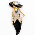 A gold and black enamel fashion brooch shaped like a woman wearing a wide-brimmed hat and a ribbon pin, embellished with clear rhinestones on a white background.