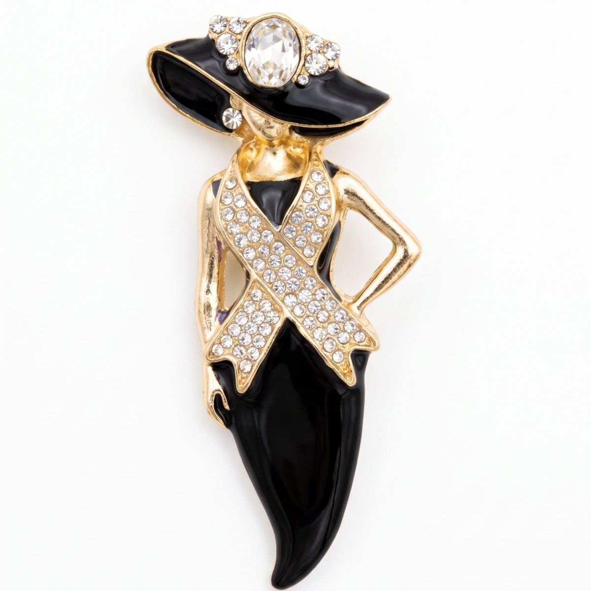 A gold and black enamel fashion brooch shaped like a woman wearing a wide-brimmed hat and a ribbon pin, embellished with clear rhinestones on a white background.