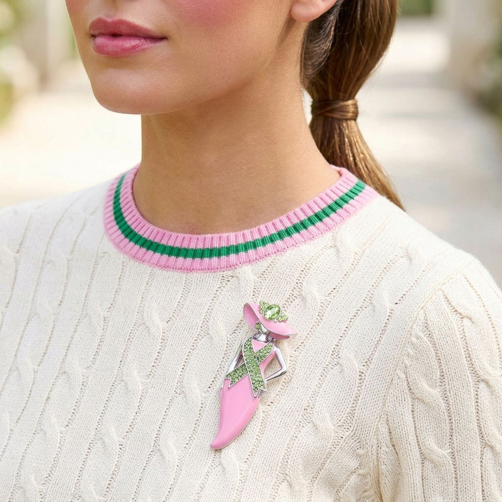 A close-up lifestyle shot of a woman wearing a pink and green ribbon-shaped brooch on her cream cable-knit sweater.