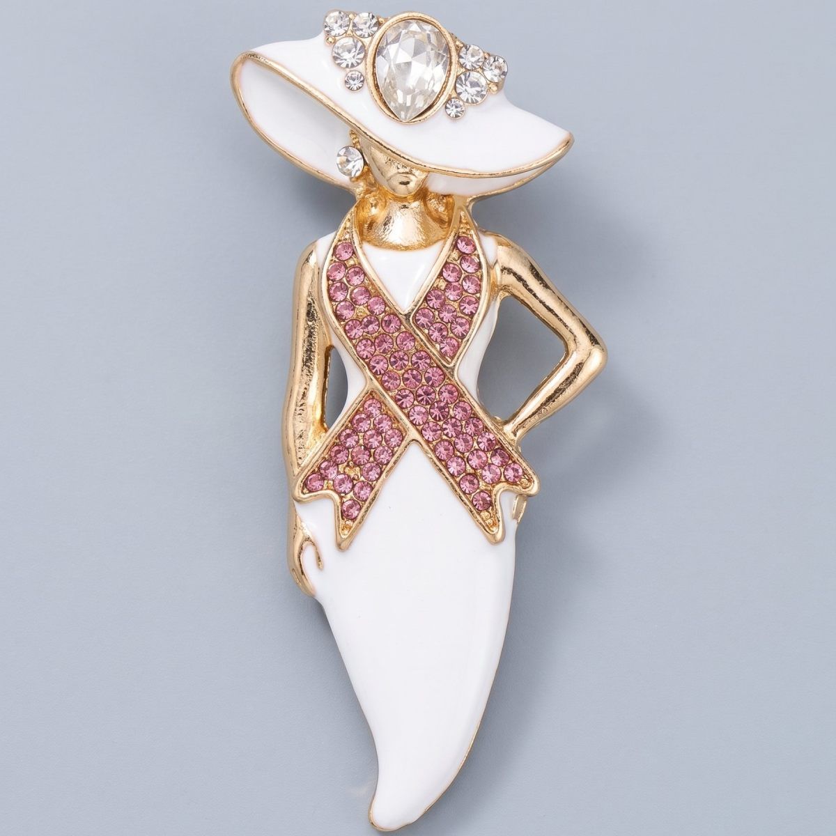 White enamel hat lady brooch in gold tone with pink rhinestone breast cancer awareness ribbon and teardrop crystal hat accent, front view on light gray background