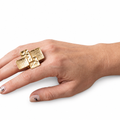 Woman’s hand wearing a gold-tone stretch statement ring with four overlapping hammered and grid-textured geometric panels on white