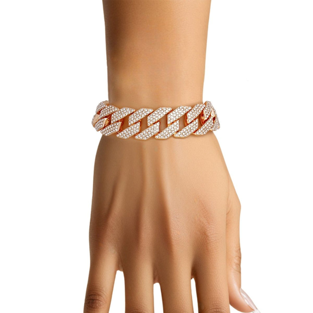 Close-up of a woman's wrist wearing a wide 14mm fully pave clear rhinestone Miami Cuban chain link bracelet in rose gold tone on a white background. The interlocking rounded links are completely covered in sparkling clear rhinestones with warm gold metal visible between the stones.