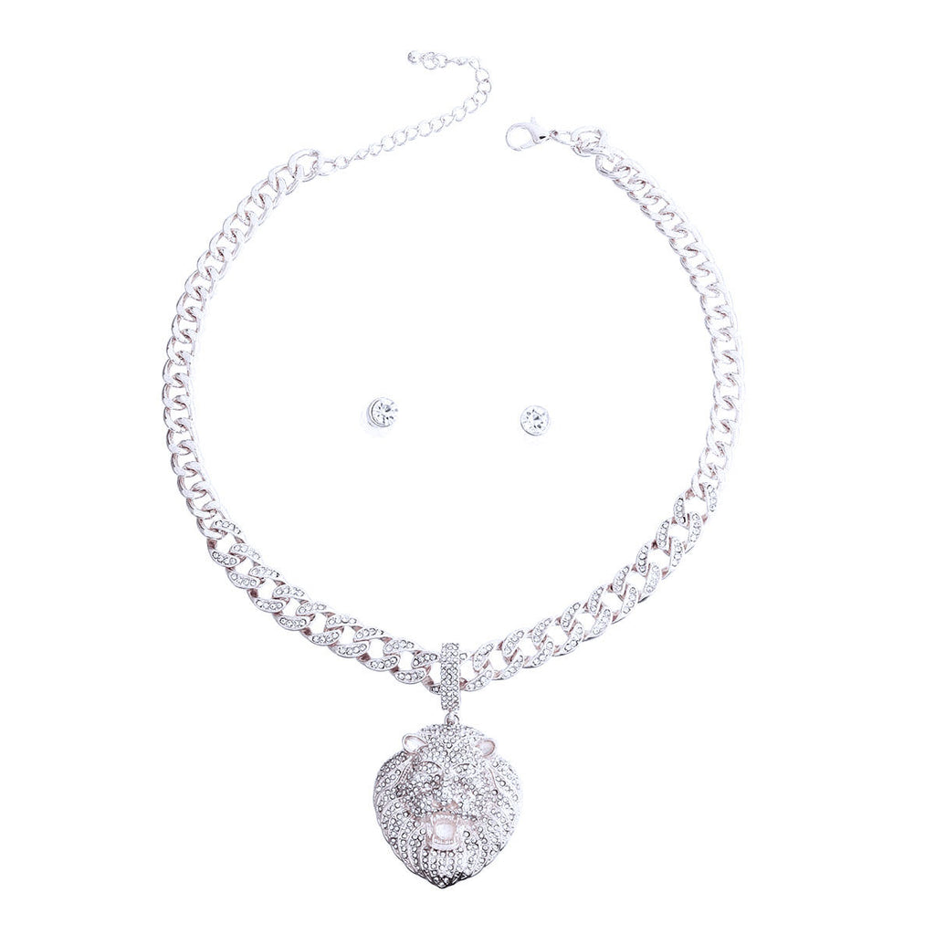 Full set on white background — rhinestone-encrusted silver Cuban link chain necklace with a large 3D rhinestone-covered lion head pendant, lobster clasp and extender chain visible, with two small round clear rhinestone stud earrings centered inside the necklace
